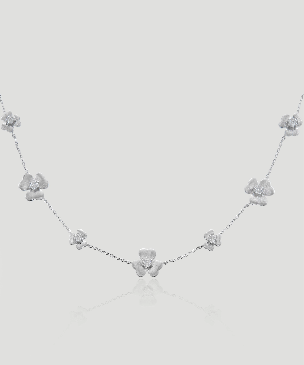 The image showcases a beautifully designed necklace named Bloom | Sterling Silver Flower Necklace. This exquisite piece is crafted from S925 Sterling Silver and adorned with sparkling 5A cubic zirconia stones. The diamond Flower necklace features a series of intricately designed flower-shaped pendants, each resembling a blooming flower with petals encrusted with zirconia, giving them a diamond-like brilliance. The flowers are evenly spaced along a delicate sterling silver chain, creating a harmonious and elegant appearance.