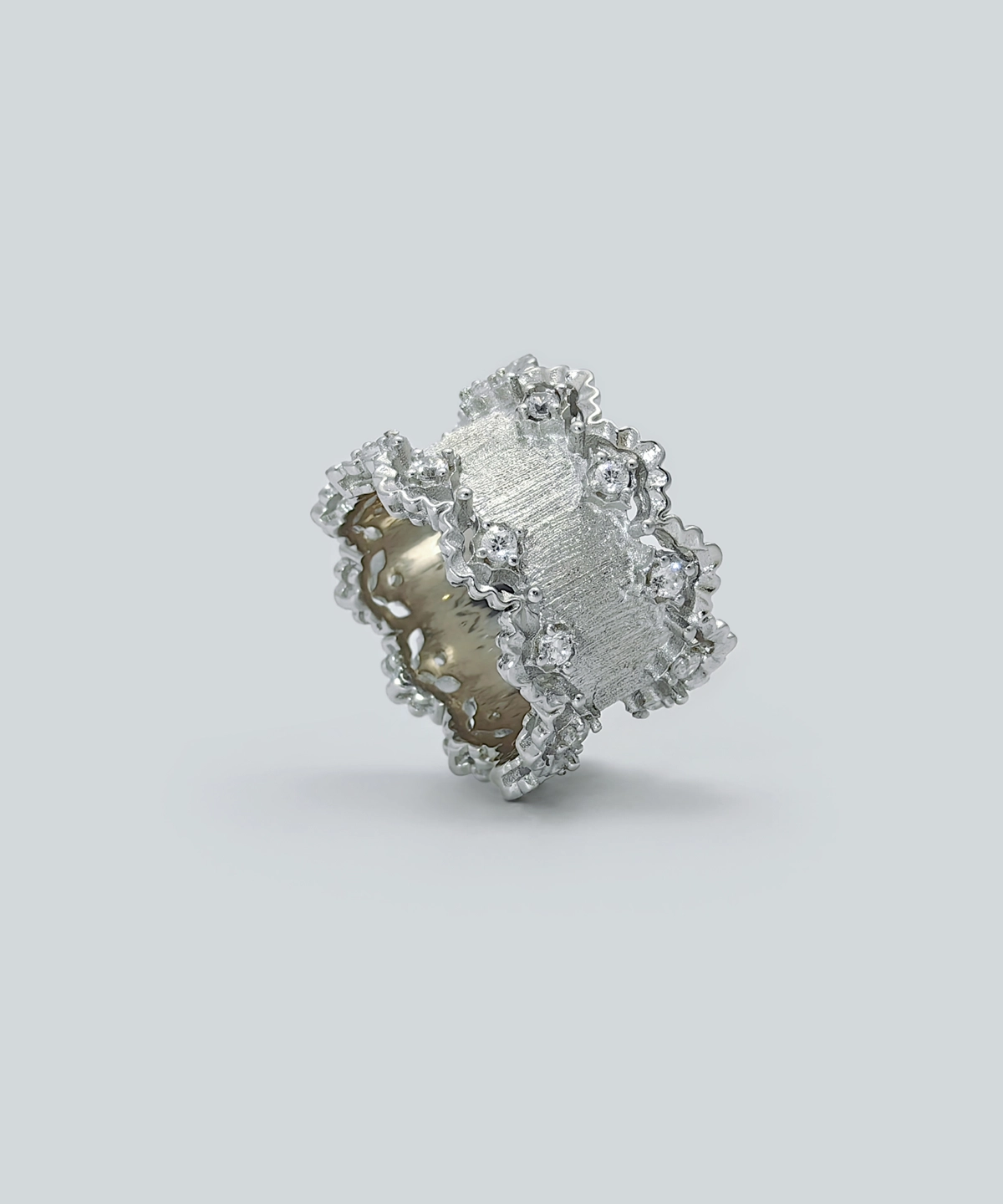The image shows a beautifully crafted Sterling Silver Lace Edge Ring, named Northern Elegance. The ring features an intricate lace edge design that adds a touch of elegance and sophistication. The surface of the ring has a textured finish, and it is adorned with small, sparkling stones embedded within the lace pattern. This Sterling Silver Ring is an ideal Christmas gift, combining timeless elegance with a unique and detailed design. The reflective surface of the ring enhances its luxurious appearance, making it a standout piece of jewelry.