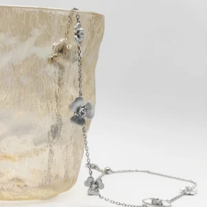 The image shows a delicate and elegant Sterling Silver Flower Necklace. The necklace is made of S925 Sterling Silver and features multiple flower-shaped pendants, each adorned with a sparkling 5A zirconia stone, resembling diamonds. The necklace is displayed draped over the edge of a textured, translucent glass vase, highlighting its intricate design and craftsmanship. The flowers are evenly spaced along the fine silver chain, showcasing the beauty and brilliance of the zirconia stones. This Diamond Flower Necklace is a stunning piece of jewelry that combines the timeless elegance of sterling silver with the dazzling sparkle of high-quality zirconia.