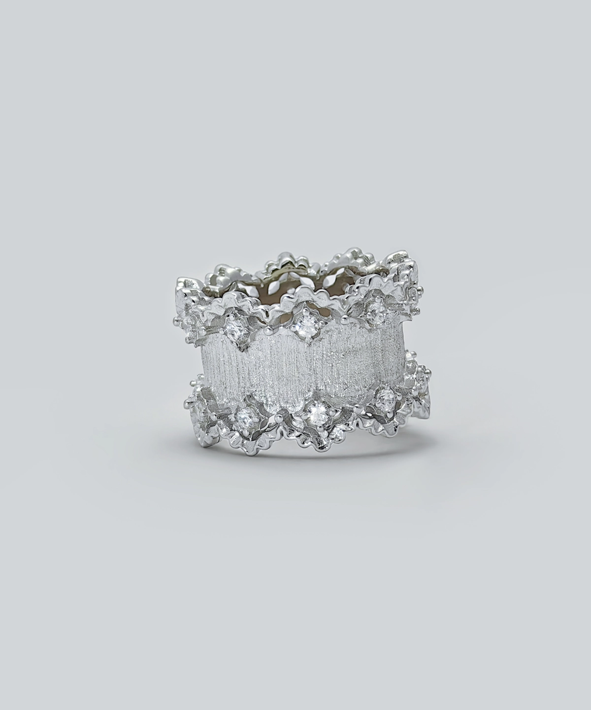 The image shows a beautifully crafted Sterling Silver Lace Edge Ring, named Northern Elegance. The ring features an intricate lace edge design that adds a touch of elegance and sophistication. The surface of the ring has a textured finish, and it is adorned with small, sparkling stones embedded within the lace pattern. This Sterling Silver Ring is an ideal Christmas gift, combining timeless elegance with a unique and detailed design. The reflective surface of the ring enhances its luxurious appearance, making it a standout piece of jewelry.