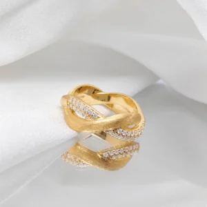 The image shows a beautifully crafted "Entwined Dimensions" ring. This intertwined ring is made of S925 sterling silver and plated with 18K gold. The design features two interwoven bands—one with a matte finish and the other adorned with sparkling 5A cubic zirconia stones. The ring is placed on a soft, white fabric, which enhances its elegance and highlights its intricate details. The perspective is slightly angled to showcase the intricate craftsmanship and the luxurious finish of the ring, making it the focal point of the image.