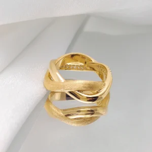 The image shows a beautifully crafted "Entwined Dimensions" ring. This intertwined ring is made of S925 sterling silver and is plated with 18K gold. It features two interwoven bands—one with a polished finish and the other with a matte finish. The ring is placed on a white surface, which highlights its intricate design and craftsmanship. The perspective showcases the elegant twist and the luxurious finish of the ring, making it the focal point of the image.