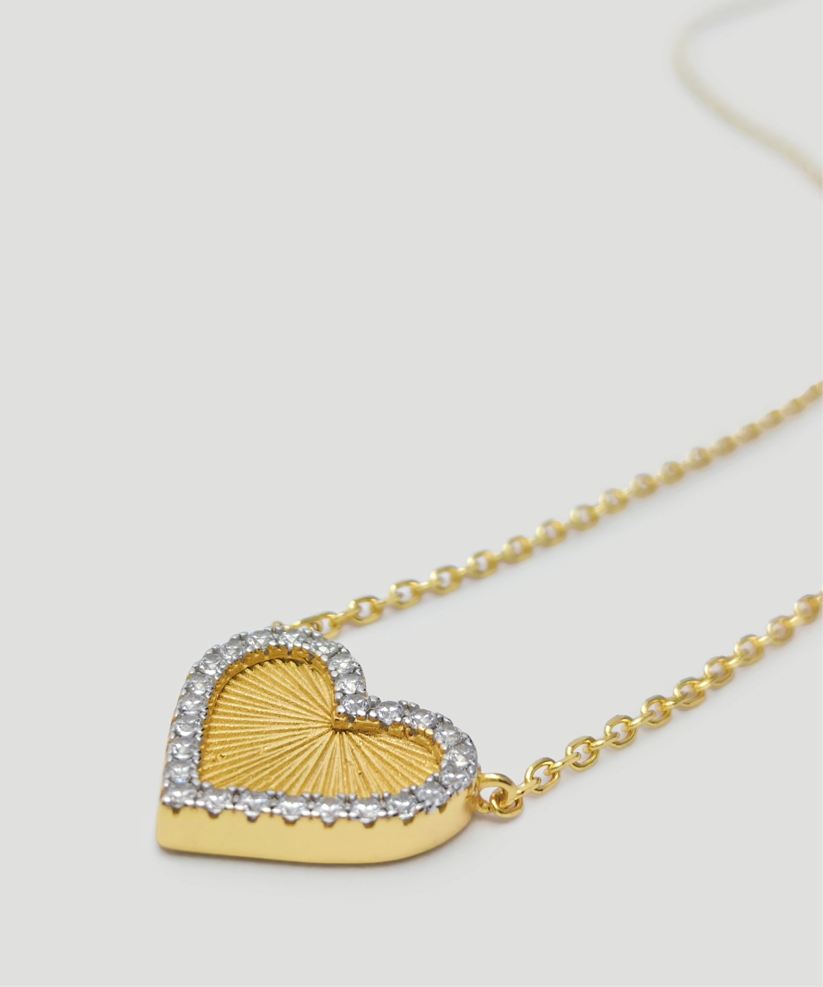 The image showcases a beautifully designed Gold Heart Pendant Necklace. This exquisite piece is crafted from S925 Sterling Silver and plated with 18K gold. The heart-shaped pendant is adorned with sparkling 5A cubic zirconia stones, adding a radiant and elegant touch. The center of the pendant features a textured gold surface, giving it a sunburst effect. The pendant is suspended from a delicate gold chain, also made from S925 Sterling Silver and plated with 18K gold. The necklace is displayed against a light-colored background, highlighting its intricate details and craftsmanship. This description includes the keywords Gold Heart Pendant Necklace and S925 Sterling Silver.