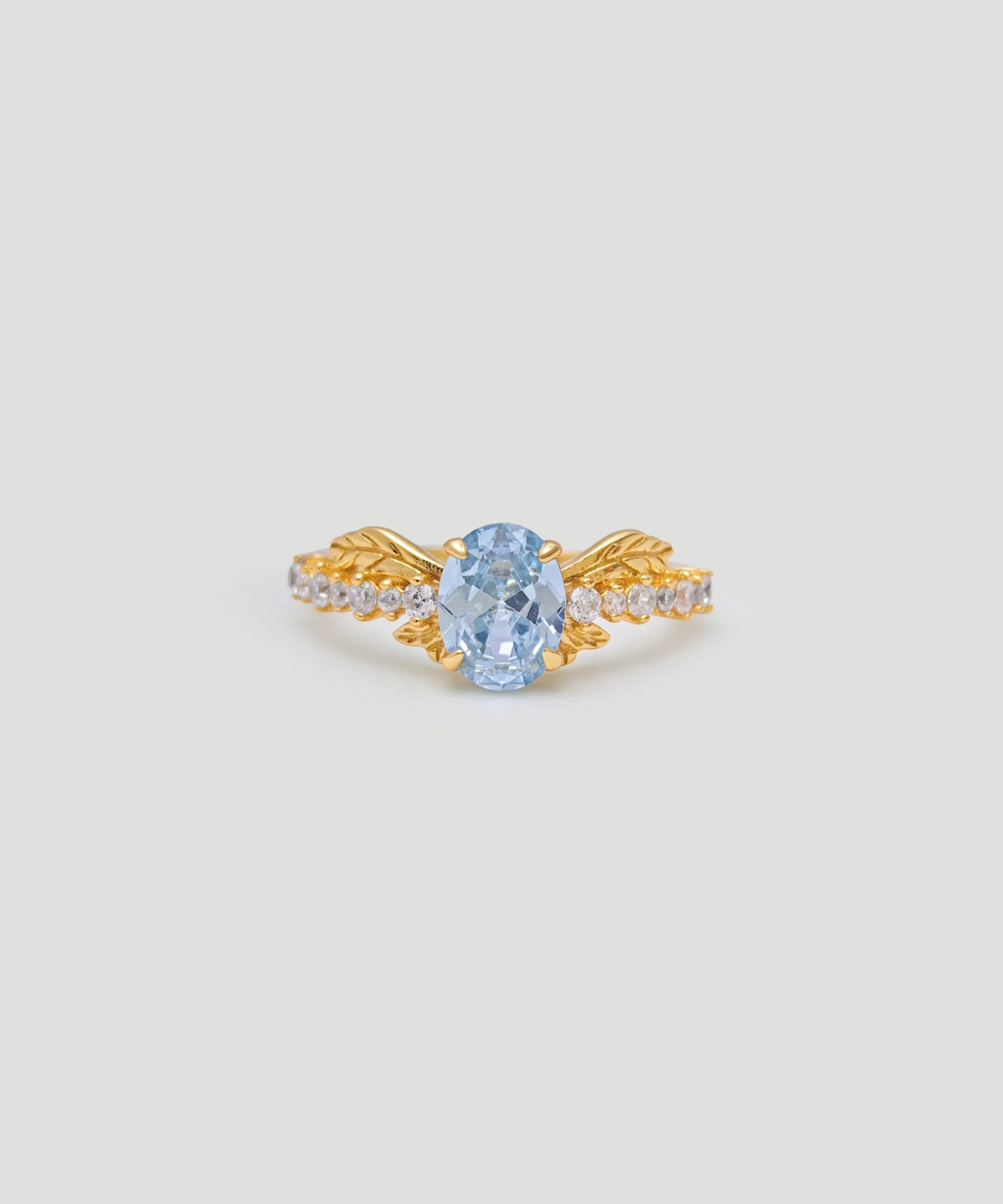 The image shows a Muse Goddess Gold Vermeil Lab Grown Sapphire Ring. This elegant ring features a central lab grown sapphire gemstone with a captivating blue hue, set within a gold vermeil band. The band is intricately designed with a series of small, sparkling 5A cubic zirconia stones that beautifully accentuate the main sapphire. Crafted from S925 sterling silver and coated with a layer of gold vermeil, the ring exudes luxury and sophistication. The ring is positioned front-facing, showcasing its detailed craftsmanship and the sparkle of the gemstones.