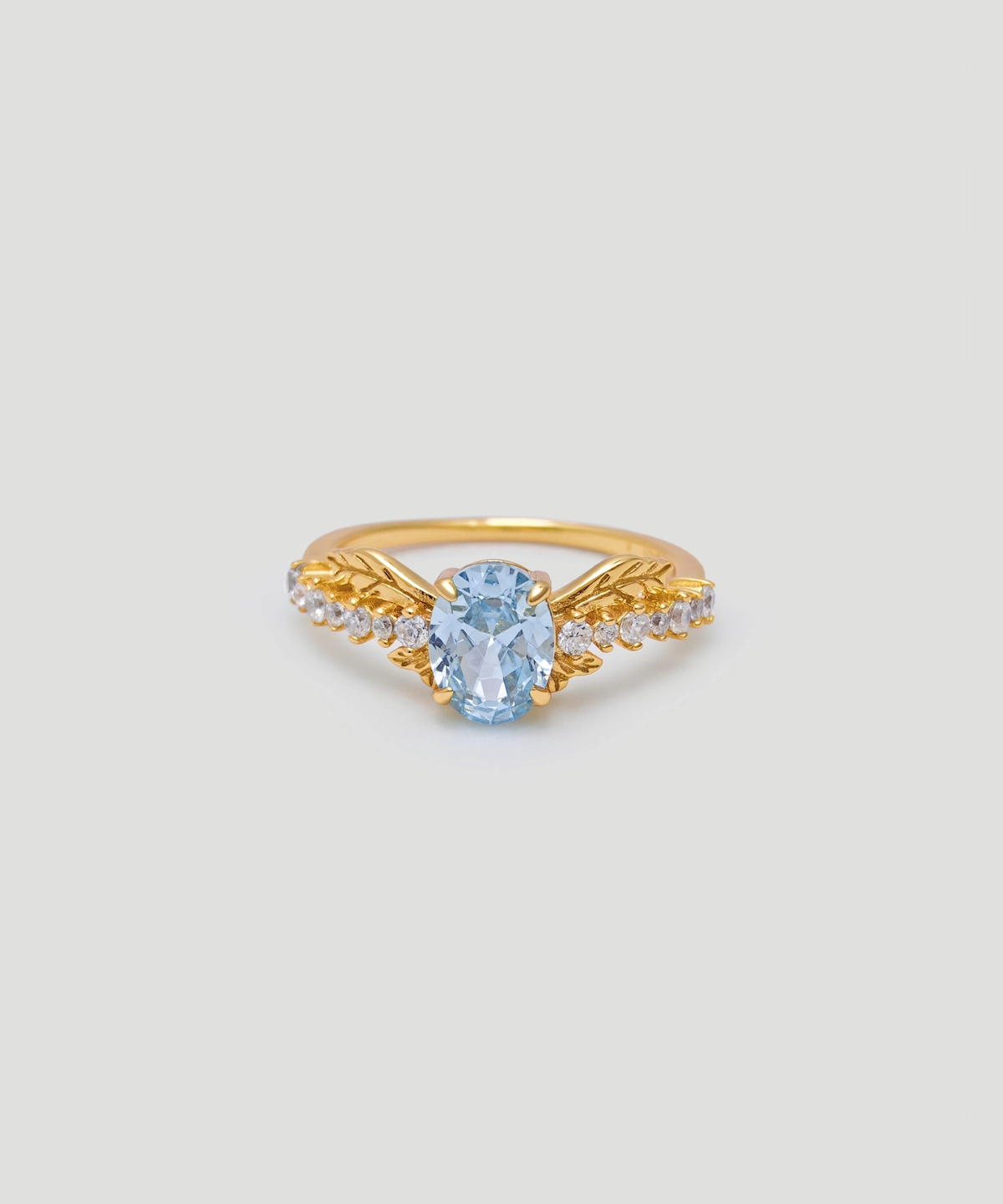 The image shows a Muse Goddess Gold Vermeil Lab Grown Sapphire Ring. This elegant ring features a central lab grown sapphire gemstone with a captivating blue hue, set within a gold vermeil band. The band is intricately designed with a series of small, sparkling 5A cubic zirconia stones that beautifully accentuate the main sapphire. Crafted from S925 sterling silver and coated with a layer of gold vermeil, the ring exudes luxury and sophistication. The ring is positioned front-facing, showcasing its detailed craftsmanship and the sparkle of the gemstones.