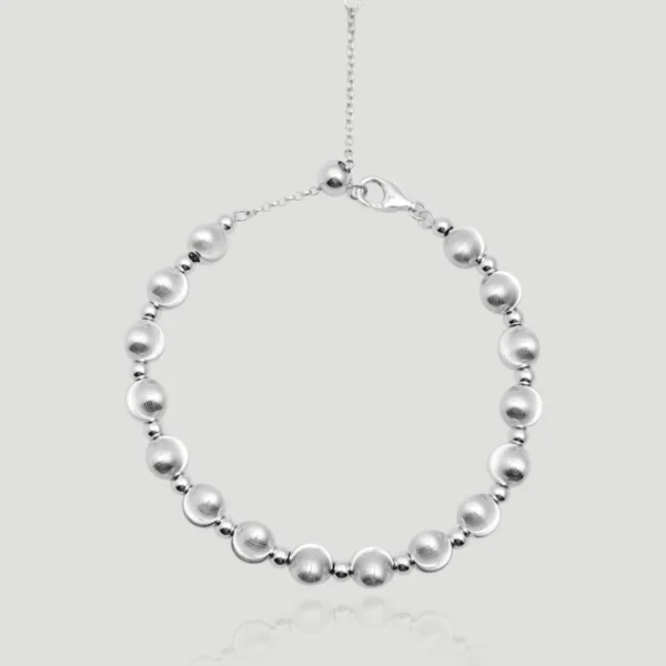 This image showcases the Silver Dreamscape Brushed Sterling Silver Ball Bracelet, elegantly crafted from S925 sterling silver. The bracelet features a sequence of brushed silver balls, interspersed with polished silver beads, creating a refined and textural contrast. The design is completed with a delicate adjustable chain adorned with a sparkling 5A-grade zircon stone at the end, adding a subtle touch of luxury. The bracelet is displayed against a soft gray background, highlighting its sleek and minimalist design. Its adjustable clasp ensures versatility for different wrist sizes, making it both functional and stylish.