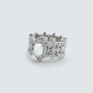 The image shows a beautifully crafted ring named Silver Moon Crown | Sterling Silver Jade Ring. The ring is made of 925 sterling silver and plated with rhodium for enhanced shine and durability. It features intricate designs with 5A cubic zirconia stones embedded throughout the band. The centerpiece of the ring is a smooth, oval-shaped Water foam jade. The ring is displayed in a way that highlights its detailed craftsmanship and the reflective quality of the sterling silver. The inner band of the ring also has a decorative pattern, adding to its overall elegance and appeal.