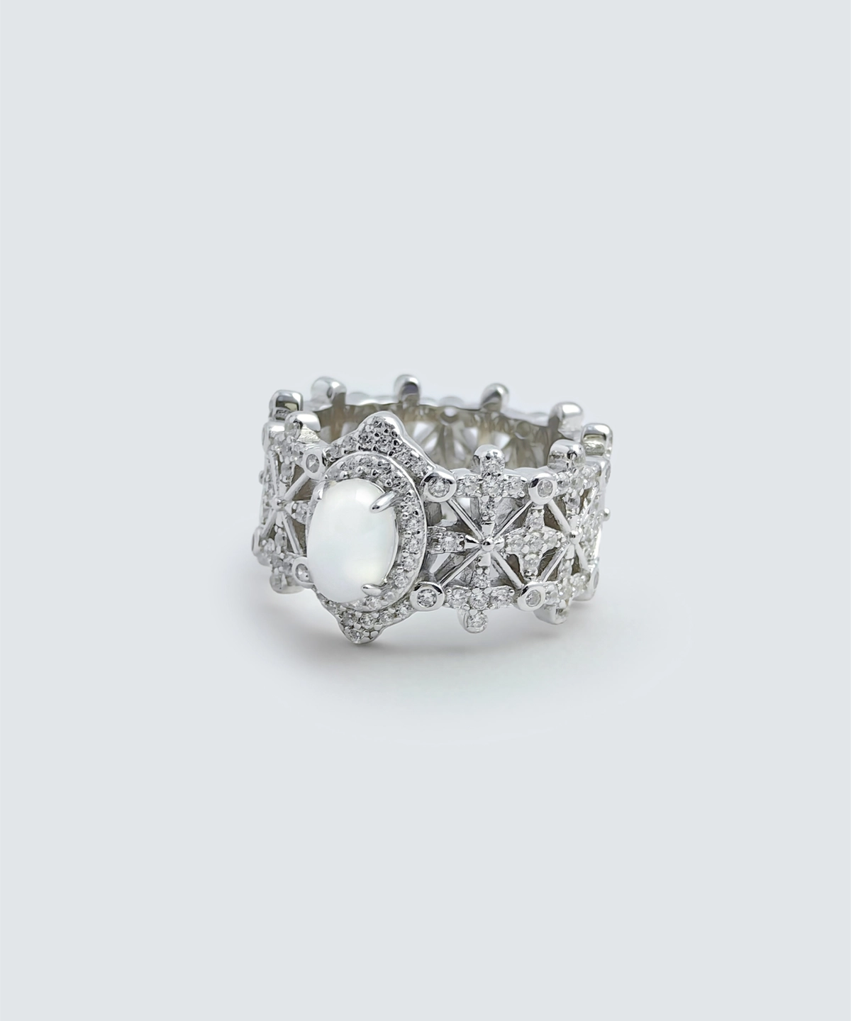 The image shows a beautifully crafted ring named Silver Moon Crown | Sterling Silver Jade Ring. The ring is made of 925 sterling silver and plated with rhodium for enhanced shine and durability. It features intricate designs with 5A cubic zirconia stones embedded throughout the band. The centerpiece of the ring is a smooth, oval-shaped Water foam jade. The ring is displayed in a way that highlights its detailed craftsmanship and the reflective quality of the sterling silver. The inner band of the ring also has a decorative pattern, adding to its overall elegance and appeal.