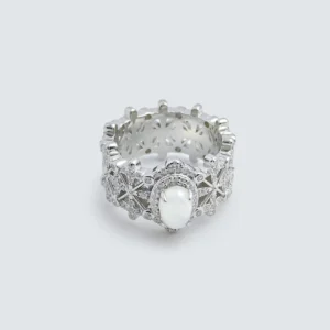 The image shows a beautifully crafted ring named Silver Moon Crown | Sterling Silver Jade Ring. The ring is made of 925 sterling silver and plated with rhodium for enhanced shine and durability. It features intricate designs with 5A cubic zirconia stones embedded throughout the band. The centerpiece of the ring is a smooth, oval-shaped Water foam jade. The ring is displayed in a way that highlights its detailed craftsmanship and the reflective quality of the sterling silver. The inner band of the ring also has a decorative pattern, adding to its overall elegance and appeal.