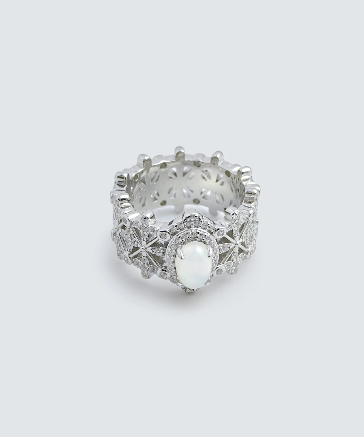 The image shows a beautifully crafted ring named Silver Moon Crown | Sterling Silver Jade Ring. The ring is made of 925 sterling silver and plated with rhodium for enhanced shine and durability. It features intricate designs with 5A cubic zirconia stones embedded throughout the band. The centerpiece of the ring is a smooth, oval-shaped Water foam jade. The ring is displayed in a way that highlights its detailed craftsmanship and the reflective quality of the sterling silver. The inner band of the ring also has a decorative pattern, adding to its overall elegance and appeal.
