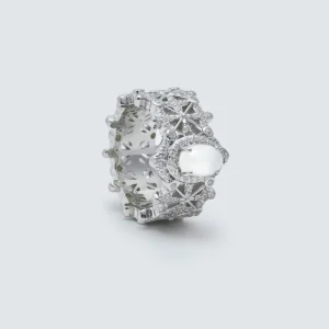 The image shows a beautifully crafted Sterling Silver Jade Ring,. The ring is made of S925 Sterling Silver plated with rhodium and is adorned with 5A cubic zirconia stones. The centerpiece of the ring features a water foam jade, which is an oval-shaped, translucent gemstone that adds a touch of elegance and sophistication. The intricate design of the ring includes detailed patterns and settings that highlight the brilliance of the zirconia stones and the jade. The ring is displayed in a close-up shot against a plain, light grey background, which emphasizes its intricate details and craftsmanship.