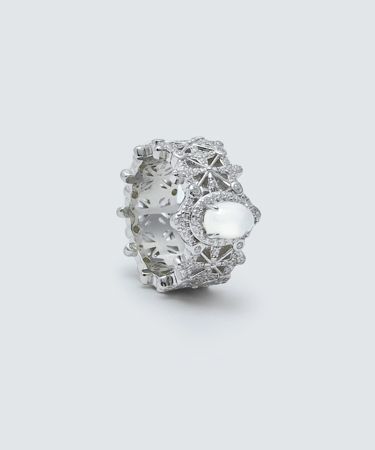The image shows a beautifully crafted Sterling Silver Jade Ring,. The ring is made of S925 Sterling Silver plated with rhodium and is adorned with 5A cubic zirconia stones. The centerpiece of the ring features a water foam jade, which is an oval-shaped, translucent gemstone that adds a touch of elegance and sophistication. The intricate design of the ring includes detailed patterns and settings that highlight the brilliance of the zirconia stones and the jade. The ring is displayed in a close-up shot against a plain, light grey background, which emphasizes its intricate details and craftsmanship.