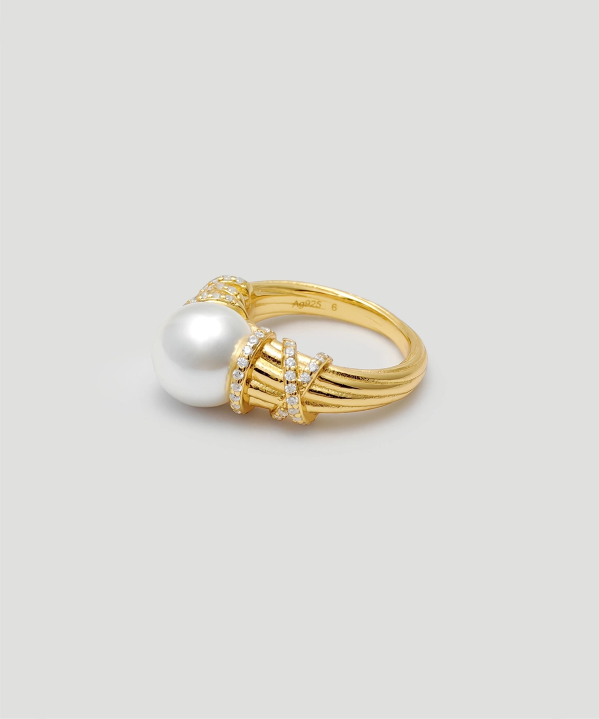 This image showcases a "Twilight" pearl ring, with the focus on the front details of the ring. The ring is made of 18k gold-plated on sterling silver. The ring's surface is embedded with a high-luster pearl. The pearl is encircled by several rows of metal bands inlaid with small diamonds, adding to the ring's luxurious appeal. The inside of the ring is marked with "Ag925," indicating its material is 925 sterling silver. The overall design is exquisite and elegant, making it suitable for various formal occasions.