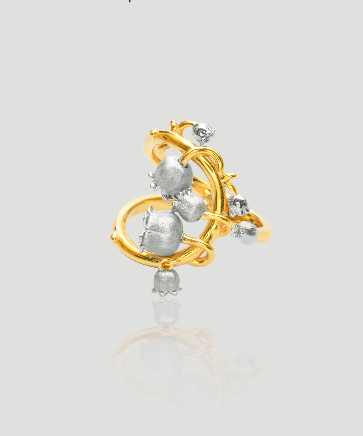 The image shows a beautifully crafted ring named Ethereal Bells | Sterling Silver Lily Of The Valley Ring. The ring features a unique design with a combination of gold-plated and sterling silver elements. The main structure of the ring is gold-plated, forming an intricate, looping pattern. Attached to this gold-plated structure are several sterling silver elements shaped like lily of the valley flowers, which are small, bell-shaped blooms. The silver flowers are distributed evenly around the gold-plated loops, creating a harmonious and elegant appearance. The ring's design is both delicate and sophisticated, making it a striking piece of jewelry.