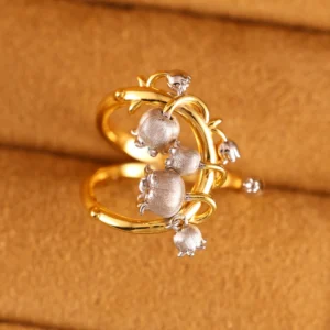 The image shows a beautifully crafted ring named Ethereal Bells | Sterling Silver Lily Of The Valley Ring. The ring features a design inspired by the lily of the valley flower, with delicate, bell-shaped flowers made of sterling silver. These flowers are attached to a gold-plated band that has an intricate, vine-like structure. The combination of the silver flowers and the gold-plated band creates a striking contrast, highlighting the detailed craftsmanship and elegance of the piece. The ring is set against a soft, beige background, which enhances the visual appeal of the jewelry. This Ethereal Bells | Sterling Silver Lily Of The Valley Ring is a stunning example of artistic design and fine materials, making it a desirable addition to any jewelry collection.