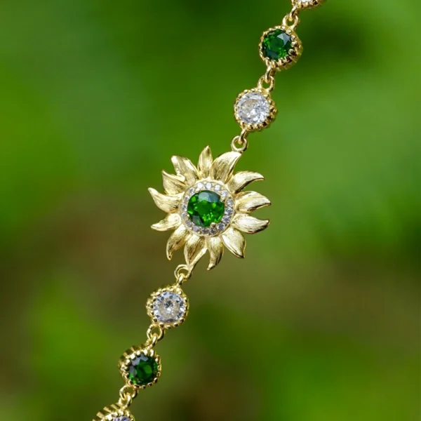 The image shows a close-up view of a beautiful Sterling Silver Sunflower Bracelet. The bracelet features a central sunflower motif, with a finely detailed sunflower crafted from sterling silver. The sunflower has intricate petals radiating outward and a textured center, capturing the essence of the flower. The bracelet chain is made up of small, round links that connect to the sunflower. The background is softly blurred, making the bracelet stand out and highlighting its delicate craftsmanship and elegant design. This Sterling Silver Sunflower Bracelet is a charming accessory that adds a touch of nature-inspired beauty to any outfit.