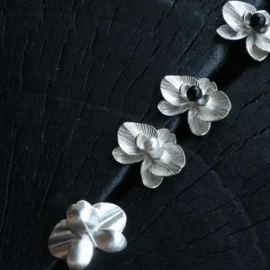 The Butterfly Orchid Earrings—delicate 925 sterling silver floral studs—celebrate nature’s elegance with refined craftsmanship. Each earring showcases an intricately sculpted orchid, accented with either a black onyx or white pearl at its center, adding contrast and sophistication. Designed for floral jewelry lovers, these earrings offer a timeless touch for casual and formal styles. The image presents them on a textured black surface, highlighting their fine details and premium quality—an ideal choice for those seeking nature-inspired luxury accessories.