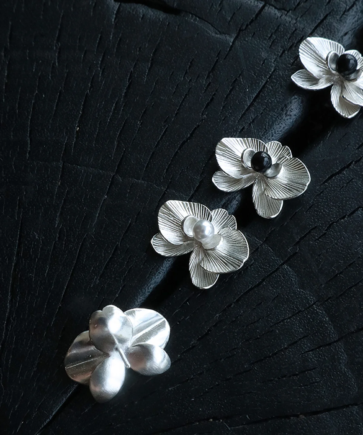 The Butterfly Orchid Earrings—delicate 925 sterling silver floral studs—celebrate nature’s elegance with refined craftsmanship. Each earring showcases an intricately sculpted orchid, accented with either a black onyx or white pearl at its center, adding contrast and sophistication. Designed for floral jewelry lovers, these earrings offer a timeless touch for casual and formal styles. The image presents them on a textured black surface, highlighting their fine details and premium quality—an ideal choice for those seeking nature-inspired luxury accessories.