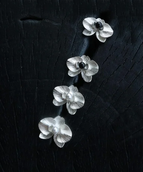 The Butterfly Orchid Earrings—delicate 925 sterling silver floral studs—blend nature-inspired elegance with refined craftsmanship. Each earring features an intricately sculpted orchid, with either a black onyx or white pearl nestled at its center, adding contrast and sophistication. Designed for floral jewelry lovers, these sterling silver studs complement both casual and formal styles. The image presents them against a textured black backdrop, accentuating their fine details—an exquisite choice for those seeking nature-inspired luxury accessories.