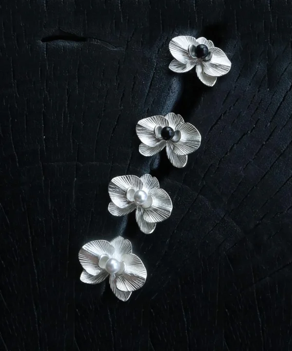 The Butterfly Orchid Earrings—delicate 925 sterling silver floral studs—blend nature-inspired elegance with refined craftsmanship. Each earring features an intricately sculpted orchid, with either a black onyx or white pearl nestled at its center, adding contrast and sophistication. Designed for floral jewelry lovers, these sterling silver studs complement both casual and formal styles. The image presents them against a textured black backdrop, accentuating their fine details—an exquisite choice for those seeking nature-inspired luxury accessories.