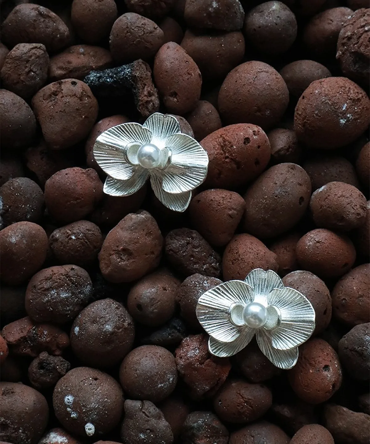 Delicate and elegant, the Butterfly Orchid Earrings are crafted from 925 sterling silver, designed to resemble blooming orchid petals. Each stud features intricate floral details and a luminous pearl at the center, exuding sophistication and natural beauty. Placed on textured brown stones, the scene emphasizes the organic inspiration behind the jewelry, creating a contrast that enhances the refined craftsmanship. Perfect for nature lovers and floral jewelry enthusiasts, these sterling silver studs add a touch of elegance to any outfit. Ideal as a meaningful gift or a statement accessory for everyday wear.