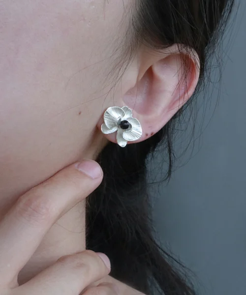 The Butterfly Orchid Earrings—elegant 925 sterling silver floral studs—gracefully frame the ear, showcasing their delicate sculpted orchid petals and black onyx center. Worn against soft lighting, the earrings subtly reflect their polished finish, adding sophistication to any style. The image captures a hand gently touching the neck, enhancing the scene’s elegance and intimacy. Perfect for floral jewelry lovers, these studs blend nature-inspired beauty with timeless craftsmanship—an exquisite accessory for both casual and formal occasions.