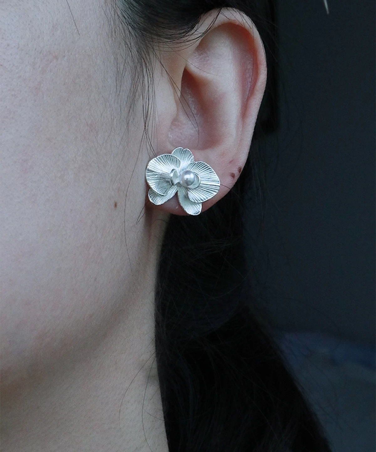 The Butterfly Orchid Earrings—exquisite 925 sterling silver floral studs—feature delicately sculpted orchid petals, with a white pearl at the center, radiating elegance and sophistication. The image captures them worn gracefully, with soft lighting accentuating their polished texture. Set against a neutral backdrop, the earrings’ intricate details and luminous finish stand out. Designed for floral jewelry enthusiasts, these sterling silver studs blend nature-inspired beauty with timeless craftsmanship—perfect for both everyday wear and formal occasions.