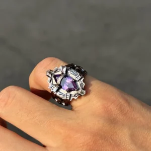 The image features a close-up view of a hand elegantly wearing the Katekyo Hitman Reborn! Vongola Ring. This exquisite piece of Handmade Anime Jewelry is crafted in sterling silver, showcasing a bold and intricate design inspired by Kyoya Hibari’s Vongola Cloud Ring. The ring’s band is detailed with sharp, angular patterns, reflecting the character’s fierce personality and adding a unique, gothic aesthetic. At the center of the ring lies a natural purple amethyst gemstone, radiating a vibrant hue that symbolizes the Cloud Flame’s strength and elegance. The polished silver surface complements the gemstone, emphasizing the artistry of this Katekyo Hitman Reborn Ring. The hand is positioned against a subtle backdrop, highlighting the ring’s craftsmanship and making it a striking accessory for fans and collectors of Vongola Rings