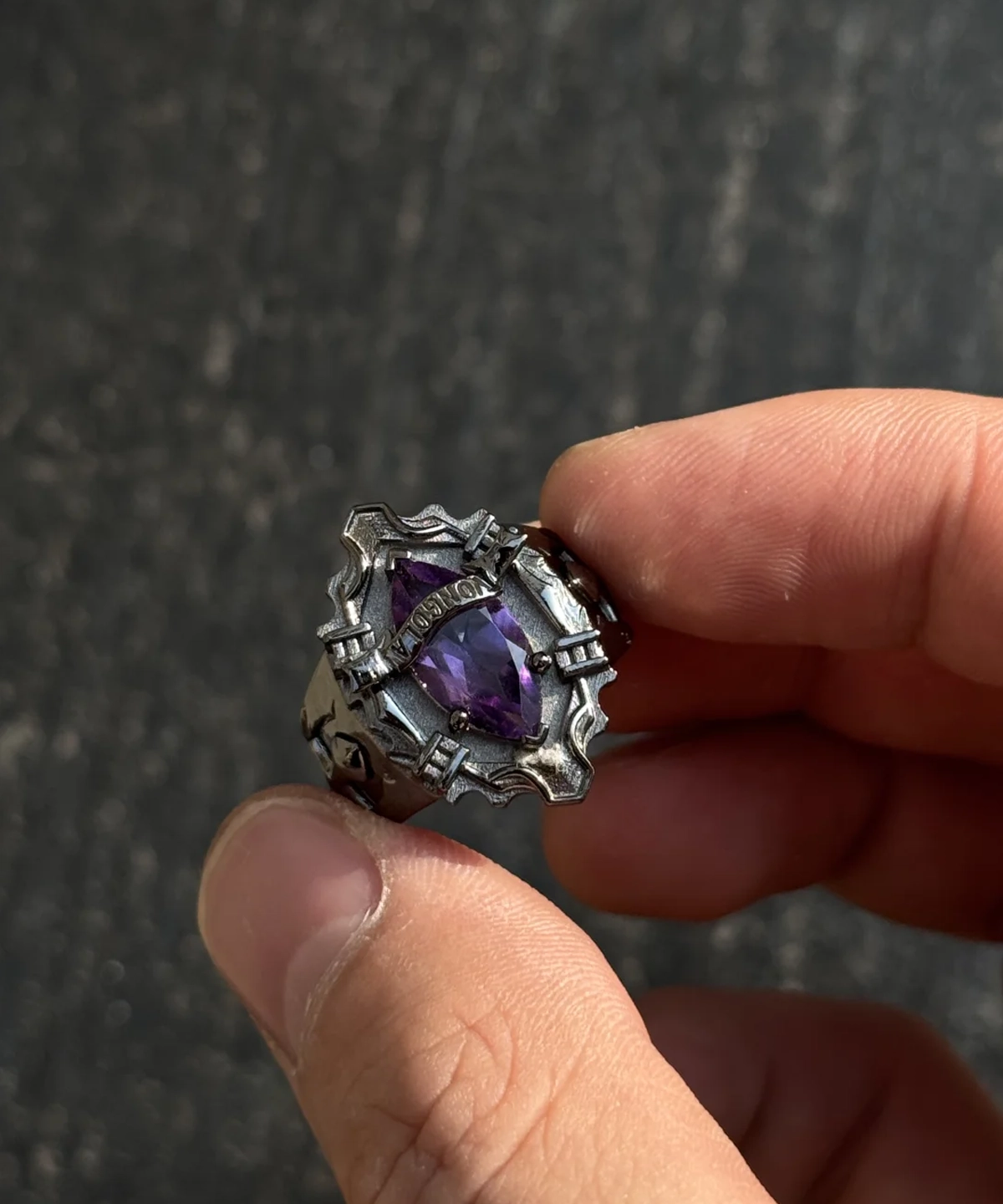 The image showcases a stunning sterling silver ring inspired by the anime Katekyo Hitman Reborn! This piece of Handmade Anime Jewelry is meticulously designed as Kyoya Hibari’s Vongola Cloud Ring. The ring features sharp, angular patterns that give it a bold and gothic look. At its center is a brilliant natural amethyst gemstone, radiating a deep purple hue that symbolizes the Cloud Flame’s power and elegance. The polished sterling silver band perfectly complements the gemstone’s vibrant color. Above the gemstone, the word "VONGOLA" is engraved, emphasizing its connection to the anime and its significance as a Katekyo Hitman Reborn Ring. The ring’s intricate craftsmanship and attention to detail make it an exceptional piece for fans and collectors of Vongola Rings.