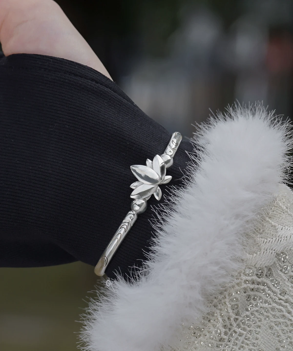The Lazesoul Handmade Anime Jewelry — 999 Pure Silver Open Adjustable Bangle, Frieren: Beyond Journey's End Mirror Lotus Bracelet, shines in its Polished Finish. The image captures it worn on a wrist, elegantly framed by a black sleeve and a soft white cuff, enhancing its refined brilliance. The sculpted lotus centerpiece and intricate engravings reflect anime artistry and fine craftsmanship. Designed for collectors and fans, this adjustable silver bangle adds a sophisticated touch to daily wear or cosplay. Set against an outdoor backdrop, the bracelet’s radiant surface gleams naturally, emphasizing purity and elegance—an essential piece for anime-inspired luxury accessories.