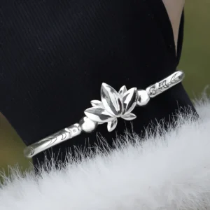 The Lazesoul Handmade Anime Jewelry — 999 Pure Silver Open Adjustable Bangle, Frieren: Beyond Journey's End Mirror Lotus Bracelet, shines in its Polished Finish. The image captures it worn on a wrist, elegantly framed by a black sleeve and a soft white cuff, enhancing its refined brilliance. The sculpted lotus centerpiece and intricate engravings reflect anime artistry and fine craftsmanship. Designed for collectors and fans, this adjustable silver bangle adds a sophisticated touch to daily wear or cosplay. Set against an outdoor backdrop, the bracelet’s radiant surface gleams naturally, emphasizing purity and elegance—an essential piece for anime-inspired luxury accessories.