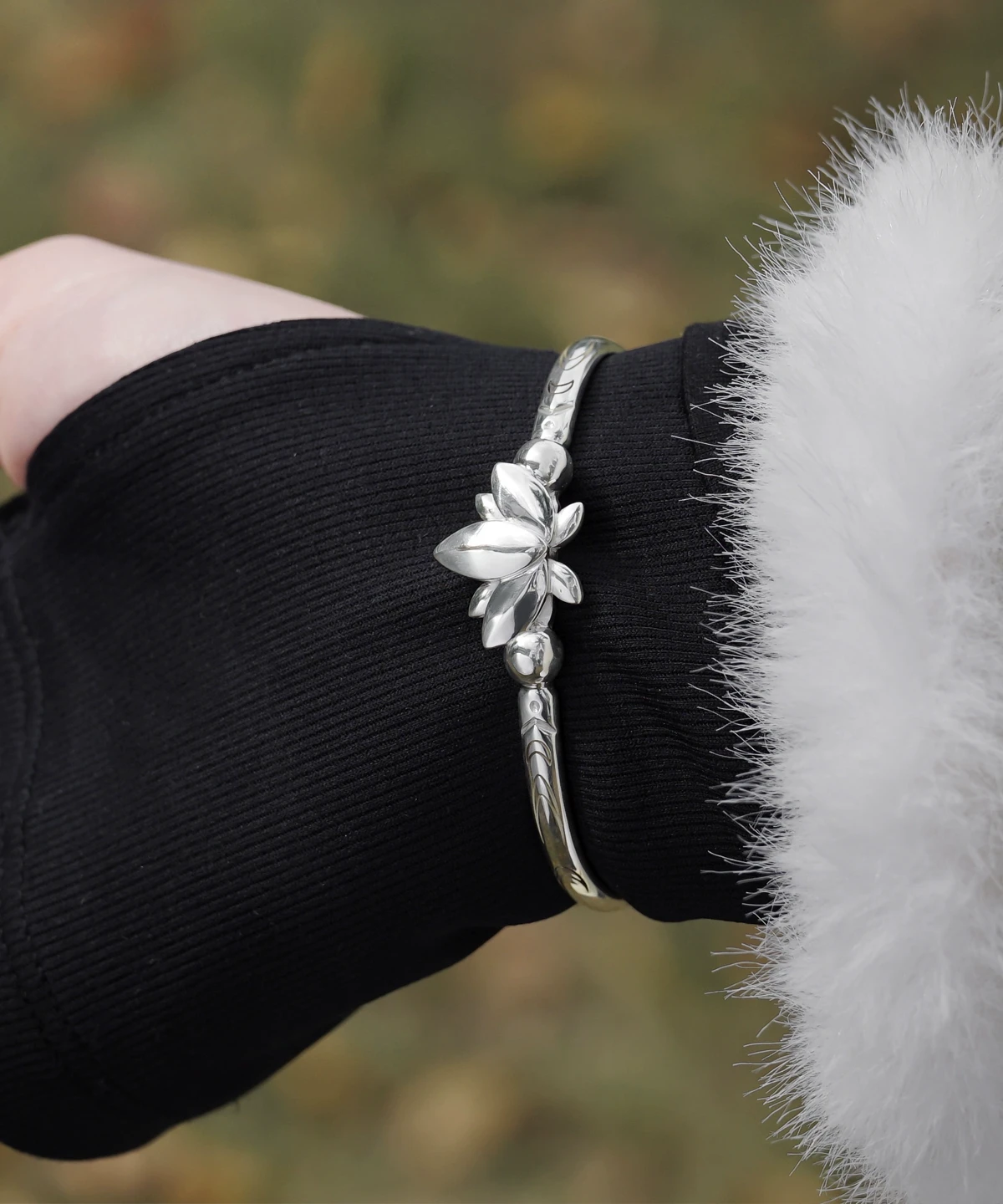 The Lazesoul Handmade Anime Jewelry — 999 Pure Silver Open Adjustable Bangle, Frieren: Beyond Journey's End Mirror Lotus Bracelet, shines in its Polished Finish. The image captures it worn on a wrist, elegantly framed by a black sleeve and a soft white cuff, enhancing its refined brilliance. The sculpted lotus centerpiece and intricate engravings reflect anime artistry and fine craftsmanship. Designed for collectors and fans, this adjustable silver bangle adds a sophisticated touch to daily wear or cosplay. Set against an outdoor backdrop, the bracelet’s radiant surface gleams naturally, emphasizing purity and elegance—an essential piece for anime-inspired luxury accessories.