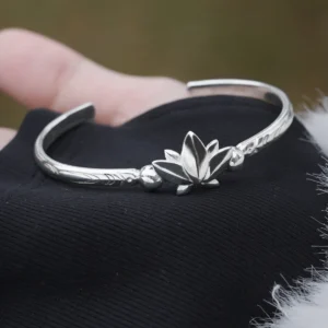 The Lazesoul Handmade Anime Jewelry — 999 Pure Silver Open Adjustable Bangle, Frieren: Beyond Journey's End Mirror Lotus Bracelet, embodies elegance and craftsmanship. Made from 999 pure silver, this bracelet features an open, adjustable design, ensuring a comfortable fit. The centerpiece is a delicately sculpted lotus flower, symbolizing purity and enlightenment, surrounded by finely engraved patterns that reflect anime artistry. Set against a black fabric backdrop, the image highlights the bracelet’s smooth texture and refined details. Perfect for anime collectors and fine jewelry enthusiasts, this exquisite piece adds a sophisticated touch to everyday fashion or cosplay.