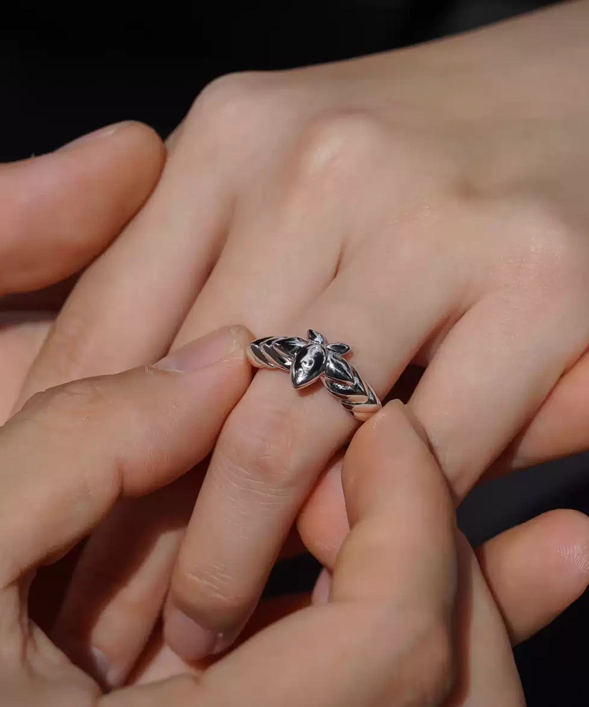 A close-up captures a tender moment as one hand gently slips the Lazesoul Handmade Mirror Lotus Ring onto another. Crafted from 999 pure silver, this open adjustable ring draws inspiration from Frieren: Beyond Journey’s End, featuring a stylized lotus motif with anime charm. Ideal for fans of fantasy jewelry and meaningful gifts.
