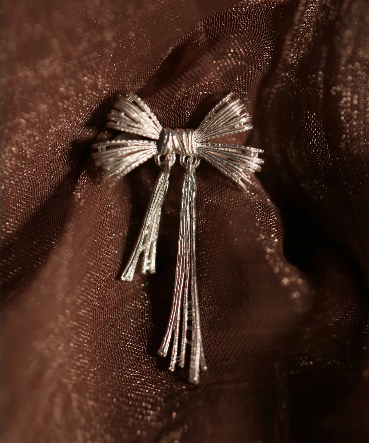 Product image of our 925 Sterling Silver Bow Ear Cuff | No Piercing Earrings displayed against a rich, textured brown fabric. The ear cuff features an elegant bow design with intricate detailing and a polished, luminous finish, embodying modern sophistication and timeless style. Ideal for trendsetters seeking stylish, non-piercing ear jewelry, this premium accessory highlights superior craftsmanship and adds a refined accent to any look.