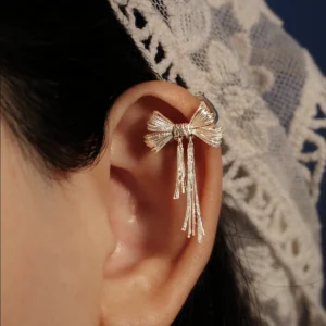 Close-up view of our 925 Sterling Silver Bow Ear Cuff | No Piercing Earrings gracefully worn on the upper ear. This delicate ear cuff features an intricately designed bow with cascading strands, highlighting refined craftsmanship and modern elegance. Set against a softly blurred backdrop, it accentuates the ear crown's contours, making it a perfect non-piercing statement accessory for both casual and formal occasions.