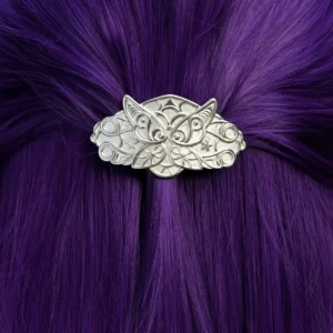 A person with long, straight, vibrant purple hair is shown from the back. Their hair is partially pulled up and secured with a detailed silver hair clip. The hair clip features an intricate design resembling elven fern motifs and is handmade from 925 sterling silver. The background consists of lush green foliage.