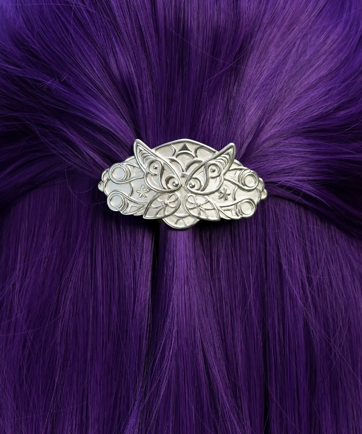 A person with long, straight, vibrant purple hair is shown from the back. Their hair is partially pulled up and secured with a detailed silver hair clip. The hair clip features an intricate design resembling elven fern motifs and is handmade from 925 sterling silver. The background consists of lush green foliage.