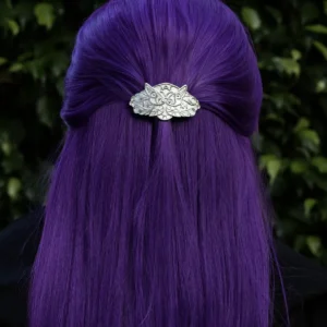 A person with long, straight, vibrant purple hair is shown from the back. Their hair is partially pulled up and secured with a detailed silver hair clip. The hair clip features an intricate design resembling elven fern motifs and is handmade from 925 sterling silver. The background consists of lush green foliage.