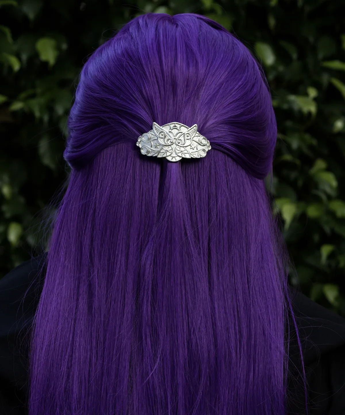A person with long, straight, vibrant purple hair is shown from the back. Their hair is partially pulled up and secured with a detailed silver hair clip. The hair clip features an intricate design resembling elven fern motifs and is handmade from 925 sterling silver. The background consists of lush green foliage.