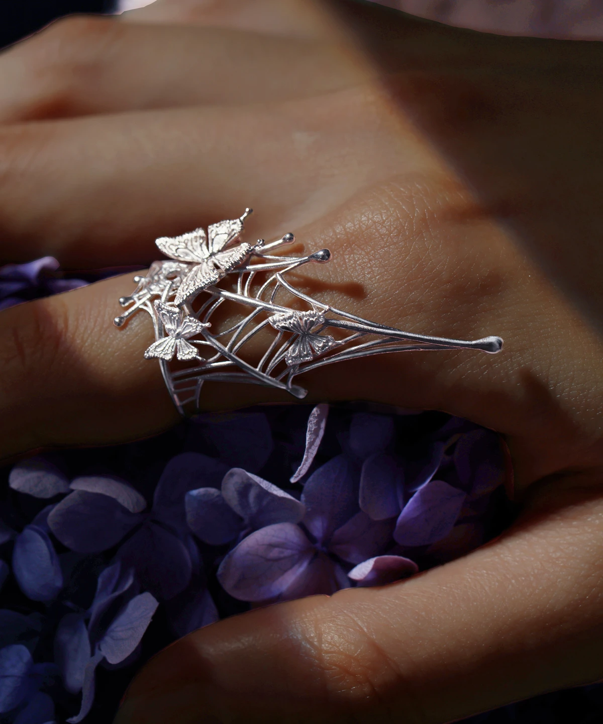 Butterfly Ring in 925 Sterling Silver | Art Fantasy Pinky Ring features an intricate spider web design adorned with delicate butterflies. Displayed on a model’s hand against a vibrant backdrop of purple blooms, this statement piece combines whimsical artistry with refined craftsmanship. Perfect for trendsetters and fashion enthusiasts, it brings a unique, fantasy-inspired touch to both casual and formal styles.