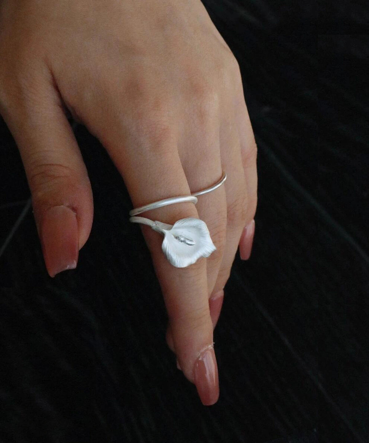 A delicate hand wears the Calla Lily Ring, a handmade, adjustable ring crafted from 999 fine silver. Inspired by the graceful calla lily flower, the design wraps elegantly around the finger, perfect for nature lovers and minimalist jewelry fans. Ideal for romantic, artistic styling.