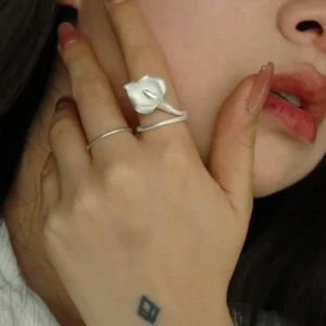 Close-up of a woman wearing the Calla Lily Ring on her index finger. The handcrafted 999 silver ring features a delicate, sculpted calla lily flower with a matte finish, wrapping elegantly around her finger. She gently touches her face with her hand, showing off the ring’s natural curves and detailed petal texture. Her minimalist style and soft expression highlight the organic elegance of the jewelry.