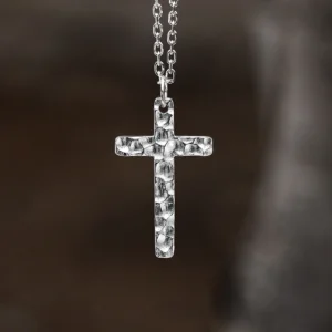 Handcrafted from 999 silver, this cross pendant features a textured, hammered finish that enhances its artisanal appeal. Suspended from an oval-link silver chain, the piece exudes understated elegance. The subtle imperfections in the metalwork highlight its handmade nature, making each pendant unique. The blurred background draws focus to the pendant’s intricate details, emphasizing its craftsmanship and refined simplicity.
