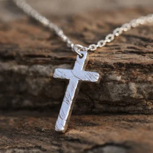 Handcrafted from 999 silver, this cross pendant features a textured surface that enhances its artisanal charm. Suspended from a delicate silver chain, it embodies elegance and craftsmanship. The rough stone background contrasts with the pendant’s polished finish, highlighting its intricate design. Ideal for those seeking a refined yet bold statement piece.