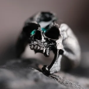Close-up view of a Dark Skull Ring crafted from S925 silver, featuring a highly detailed skull design with a green gemstone inlay set in one eye socket. The ring’s dark, edgy aesthetic enhances its bold and unconventional style.