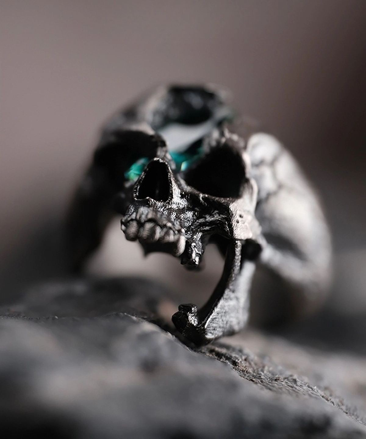 Close-up view of a Dark Skull Ring crafted from S925 silver, featuring a highly detailed skull design with a green gemstone inlay set in one eye socket. The ring’s dark, edgy aesthetic enhances its bold and unconventional style.