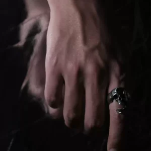 A close-up of a hand wearing the Dark Skull Ring – S925 Silver with Gemstone Inlay. The ring showcases an intricately carved skull motif, accented with a gemstone inlay for a bold, gothic aesthetic.