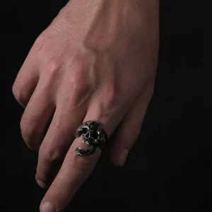 A close-up of a hand wearing the Dark Skull Ring – S925 Silver with Gemstone Inlay. The ring showcases an intricately carved skull motif, accented with a gemstone inlay for a bold, gothic aesthetic.