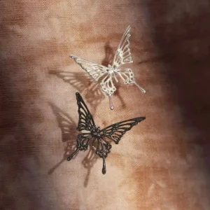The image features two pairs of Dream Butterfly Earrings & Ear Cuffs, one in silver and the other in black, elegantly displayed against a textured brown background. These butterfly earrings are designed to be worn without piercings, offering a delicate yet bold aesthetic.